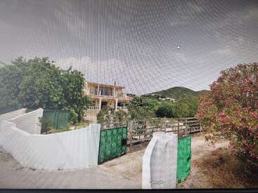 L'image représente une maison sereine à deux étages avec un balcon, entourée d'arbres luxuriants et d'une clôture blanche, sur fond de ciel nuageux.