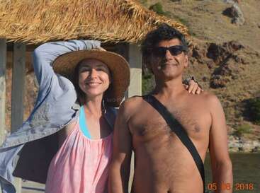 L'image montre un homme et une femme posant pour une photo sur une plage, la femme portant un chapeau de paille et l'homme étant torse nu.