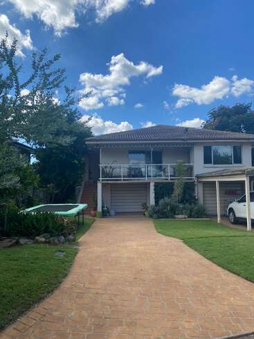 Una casa moderna de dos plantas con tejado de tejas, entrada de ladrillo, cama elástica, césped verde, plantas, coche blanco, cielo azul y nubes blancas dispersas. Ambiente atractivo.