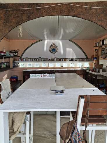 This cozy kitchen features a large white table, shelves of jars, and a peacock feather mural. A sign reads, "Cooking is form of ART."