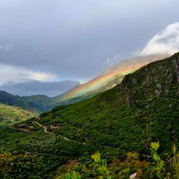 Lush green mountains stretch beneath a cloudy sky, while a vibrant rainbow arcs gracefully across the landscape, illuminating the scenery with colorful, natural beauty and wonder.