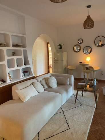 Un salon confortable avec un canapé beige clair, une décoration moderne, des miroirs ronds, des étagères encastrées, un petit coin repas, un éclairage chaleureux et des accents naturels et terreux.