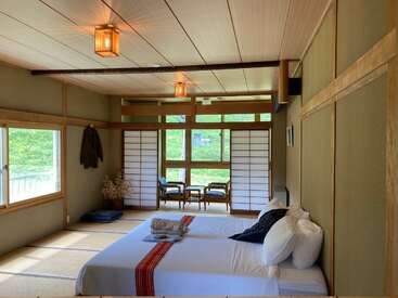 Das Bild zeigt ein ruhiges Schlafzimmer mit einem großen Bett, hölzernen Akzenten und einer Schiebetür, die auf eine Terrasse führt und ein Gefühl von Ruhe und Gelassenheit vermittelt.