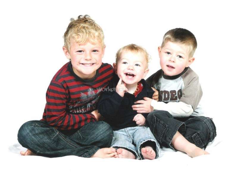 The image depicts three young boys sitting together, with the middle child being held by the boy on the left and the boy on the right sitting beside him.