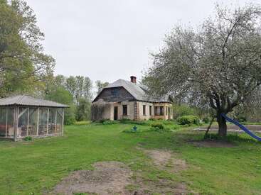 A rustic house stands surrounded by trees and green grass. Nearby, a screened gazebo and a tree with a blue slide create a peaceful, rural atmosphere.