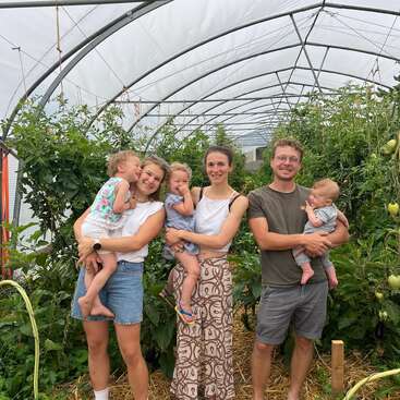 Une famille heureuse se tient réunie dans une serre luxuriante, entourée de grandes plantes. Les adultes tiennent dans leurs bras des enfants souriants, créant ainsi une atmosphère chaleureuse, joyeuse et pleine d'amour.