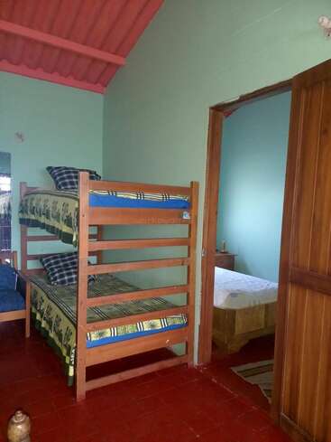 Cette chambre confortable dispose d'un lit superposé en bois avec une literie colorée, d'un sol carrelé rouge, de murs verts et d'une porte ouverte menant à une autre chambre simple.