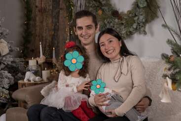 Eine glückliche vierköpfige Familie sitzt gemeinsam auf einem gemütlichen Sofa, umgeben von festlicher Weihnachtsdekoration, und lächelt herzlich. Die Gesichter der Kinder sind mit Blumenaufklebern verziert.