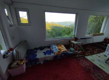 Ein gemütliches Zimmer mit großen Fenstern bietet einen atemberaubenden Blick auf die Berge. Die schlichte Einrichtung besteht aus einem Bett, bunten Decken, Spielzeug, Pflanzen und weichen Teppichen, was eine friedliche Atmosphäre schafft.