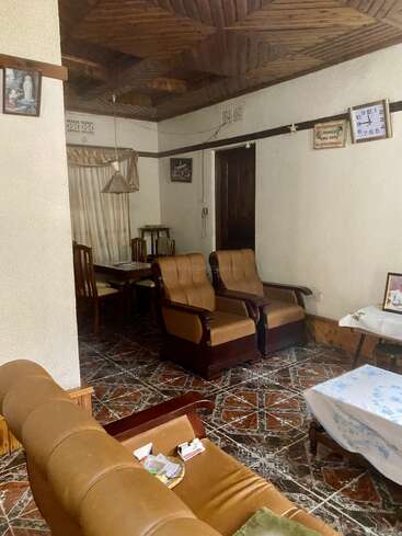 Esta imagen muestra un acogedor salón con sillas de cuero marrón, techo de madera, suelo de baldosas, reloj de pared, mesa de comedor, cuadros enmarcados y manteles decorativos.