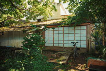 The image depicts a serene outdoor scene featuring a house with a large yard, surrounded by trees and a fence, with a clear sky and a body of water in the background.