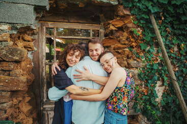 Three individuals are embracing each other, with their arms around one another\'s backs, conveying a sense of unity and support. The scene is set against a neutral background.