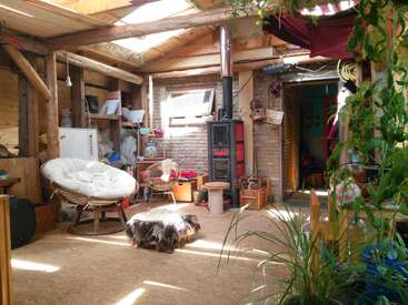 Cette chambre rustique et confortable est dotée de poutres apparentes, d'un poêle à bois, d'une lumière naturelle, de sièges éclectiques, de plantes d'intérieur et d'une décoration naturelle, créant une atmosphère chaleureuse, accueillante et conviviale.