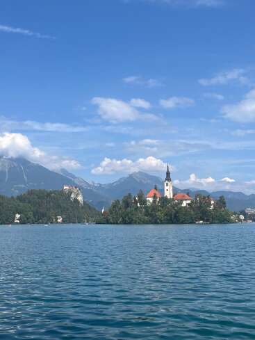 Un lac bleu serein avec une île pittoresque où se trouve une église. Les montagnes et les nuages forment une toile de fond étonnante, mettant en valeur le paysage naturel paisible et pittoresque.