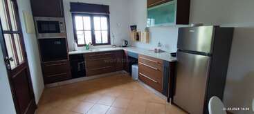 Esta imagen muestra una cocina moderna con armarios marrones, electrodomésticos de acero inoxidable, frigorífico, microondas, horno, fregadero, tetera, ventana, suelo de baldosas y accesorios de encimera.