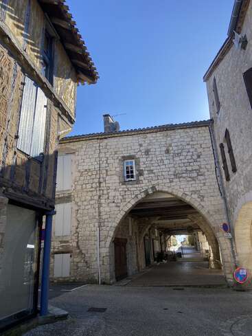 Cette image montre une charmante rue européenne historique, avec ses bâtiments en pierre, ses poutres apparentes, ses passages voûtés et son ciel bleu limpide, qui évoque une atmosphère paisible d'antan.