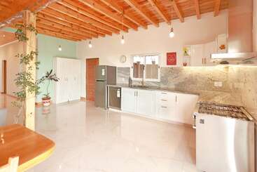 Essa cozinha moderna tem armários brancos, eletrodomésticos de aço inoxidável, bancadas de mármore e teto de madeira. É espaçosa, iluminada, com decoração minimalista, plantas e luminárias elegantes.