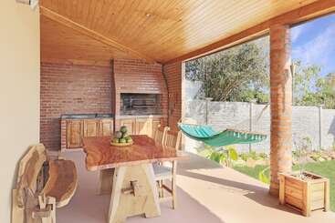 Este aconchegante pátio externo tem teto de madeira, churrasqueira rústica de tijolos, mesa e bancos de madeira natural, rede, vista para o jardim e muita luz solar. O refúgio perfeito.