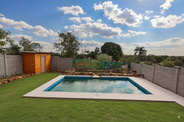 A rectangular swimming pool sits in a neatly mowed backyard, surrounded by a concrete border, stone wall, wooden shed, and colorful nature-themed mural.