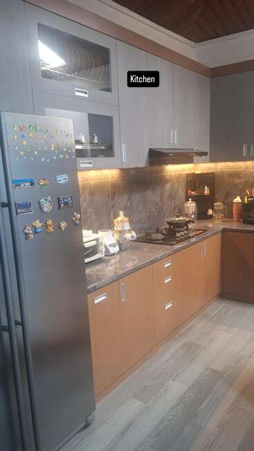 A modern kitchen with grey cabinets, a fridge decorated with magnets, countertop appliances, gas stove, and under-cabinet lighting. The word "Kitchen" is labeled above.