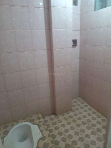 This image shows a tiled bathroom with a squat toilet in the floor, pink wall tiles, patterned floor tiles, and a small corner section separated by a wall.