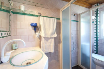 The image depicts a bathroom with a shower, sink, and toilet, featuring white walls and a tiled floor, with a large mirror and a window, providing a clean and organized space.