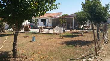 A imagem retrata uma cena serena ao ar livre, com uma casa com um quintal cercado, uma árvore e um corpo d'água, evocando uma sensação de tranquilidade e beleza natural.