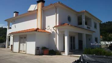 Das Bild zeigt ein modernes Haus mit einem großen Fenster und einer kleinen Veranda, mit einem gepflegten Rasen und einer Auffahrt, vor dem Hintergrund eines klaren blauen Himmels.