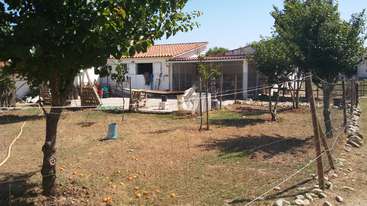 A imagem retrata uma cena serena ao ar livre, com uma casa com um quintal cercado, uma árvore e um corpo d'água, evocando uma sensação de tranquilidade e beleza natural.