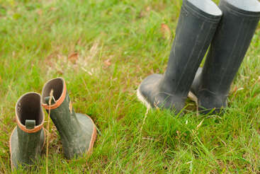 Deux paires de bottes en caoutchouc, l'une verte et l'autre noire, sont posées sur un sol herbeux, suggérant une activité de plein air ou de jardinage dans un cadre naturel et rural.