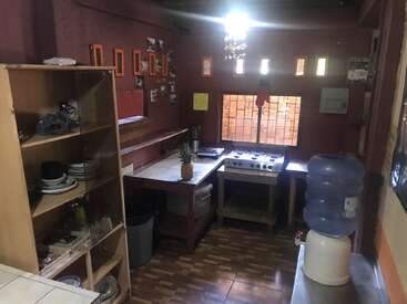 Esta acogedora cocina cuenta con paredes rojas, estantes con vajilla, una cocina de gas, un dispensador de agua, fotos enmarcadas, un centro de mesa con una piña y superficies de azulejos y madera.