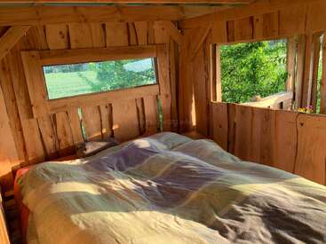 Ein gemütliches Schlafzimmer in einer Holzhütte mit großen Fenstern, einem Doppelbett, sanftem Licht und einem wunderschönen Blick auf die grüne Landschaft, die sich durch die weitläufige Aussicht auf die Natur bietet.