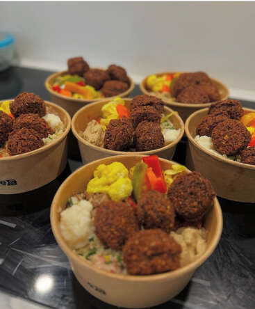 Sechs Schüsseln mit Falafel, eingelegtem Gemüse und Salat stehen ordentlich auf einem Tisch und zeigen ein farbenfrohes, gesundes und appetitliches mediterranes Essen.