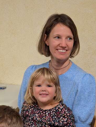 Una mujer sonriente con un top azul claro se sienta detrás de una alegre joven con un vestido de flores. Ambas parecen felices, compartiendo un alegre momento juntas.
