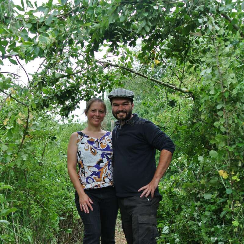 The image depicts a man and woman standing together in a lush green forest, surrounded by trees and foliage, with a serene and natural atmosphere.