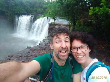 La imagen muestra un selfie de un hombre y una mujer frente a una cascada, con la fecha "30.10.20" en amarillo en la esquina inferior derecha.