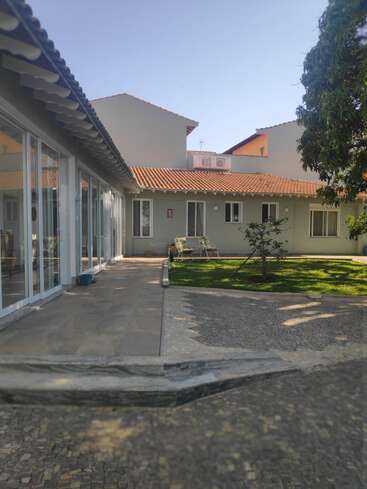 Dieses Bild zeigt ein modernes Haus mit Ziegeldach, großen Fenstern und einem großen Innenhof. Es gibt grünes Gras, Bäume, Bänke und sonniges Wetter.