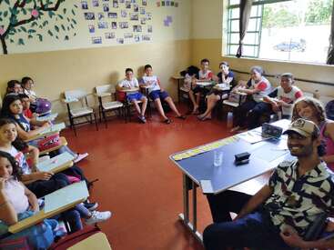 Ein fröhliches Klassenzimmer voller Schüler und einer Lehrerin, die im Halbkreis angeordnet sind. Bunte Wände, lächelnde Gesichter und Sonnenlicht schaffen eine lebendige, ansprechende Lernumgebung.