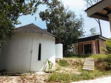 Dieses Bild zeigt ein rundes weißes Gebäude mit einem schrägen Dach, ein modernes Backsteinhaus, üppiges Grün, Bäume, blauen Himmel und eine Freitreppe an einem sonnigen Tag.