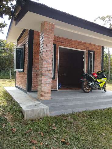Ein kleines, gemauertes Haus mit einer Veranda steht auf einer Wiese. Ein geparktes Motorrad steht auf der Veranda. Die Fenster sind offen, umgeben von Bäumen.