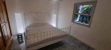 Das Bild zeigt ein Zimmer mit einem Bett, einem Tisch und Stühlen, mit einem großen Fenster und einer Tür, mit einer weißen Wand und einem grauen Boden, der einen sauberen und organisierten Raum darstellt.