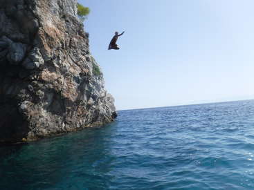 Une personne saute d'une falaise rocheuse dans l'océan, les bras tendus et les jambes pliées, créant une éclaboussure dans l'eau en contrebas.