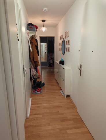 This hallway features wooden flooring, white walls, a hanging coat rack, shoes, a console table, a round mirror, small framed pictures, and modern lighting.