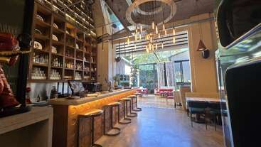 This modern bar features a stylish counter with high stools, a tall shelf of bottles, contemporary lighting, and large windows offering a bright, inviting atmosphere.