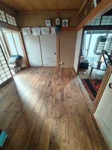 This image shows a traditional Japanese room with wooden flooring, sliding shoji doors, hanging papers, simple furniture, and a cozy adjacent room with a round table.