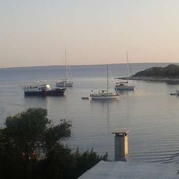 The image depicts a serene coastal scene, featuring a tranquil body of water dotted with boats, a chimney, and trees, set against a clear sky.