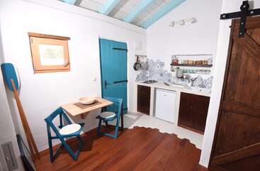 This cozy kitchen features a small dining area with blue chairs, compact appliances, wooden accents, patterned backsplash, and nautical decor, creating a charming, cottage-like atmosphere.