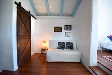 A cozy nook features a white loveseat with patterned pillows, a small wooden table with a lamp, wall art, wooden floors, a rustic sliding barn door, and blue ceiling beams.