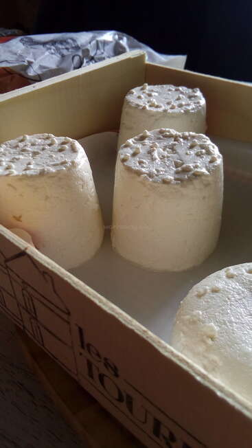 L'image montre une boîte de quatre fromages blancs cylindriques à la texture rugueuse, posés sur une surface blanche, peut-être dans une cuisine ou une zone de préparation des aliments.