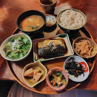 Ein traditionelles japanisches Essensset mit gegrilltem Fisch, Miso-Suppe, Reis, Salat, eingelegtem Gemüse, gekochten Wurzeln und Seetang, alles schön auf einem Holztablett angerichtet.